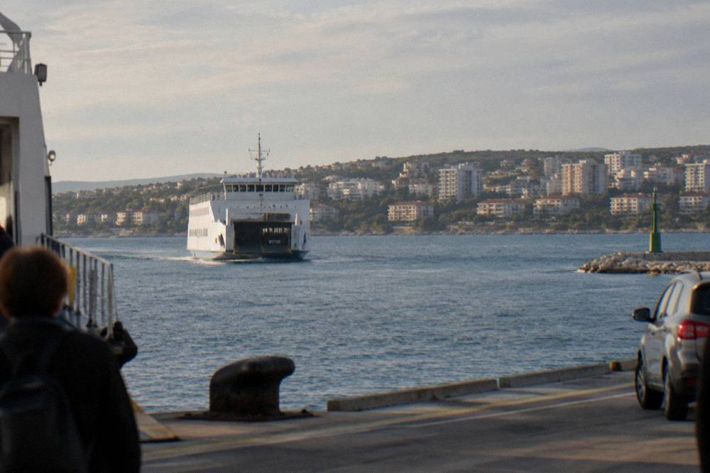 A ferry approaching the port with apartment blocks on the hillside beyond.