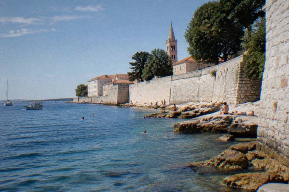 Swimmers drying on seaside stones below the old walls of Zadar.