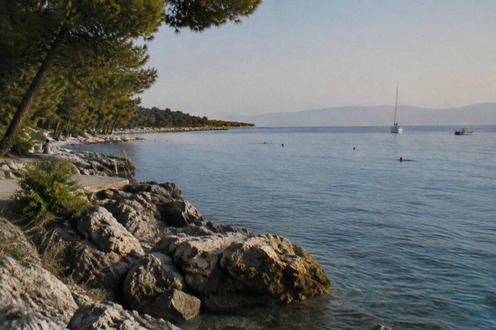 A stone headland beach with an open sea horizon and a few distant bathers.