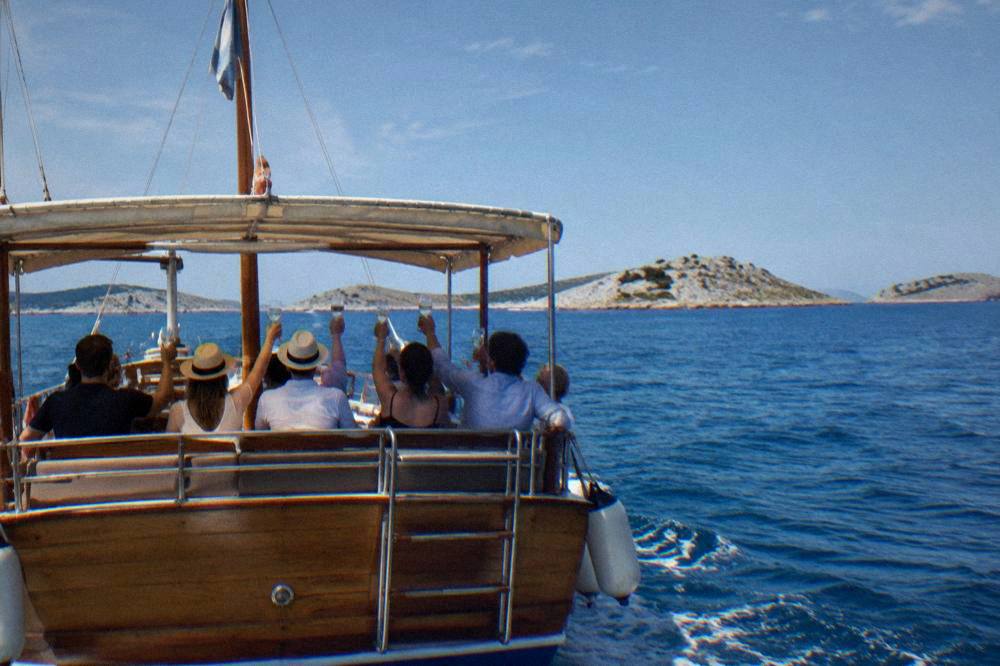 A traditional wooden boat with passengers seen from behind at the stern on a blue sea.