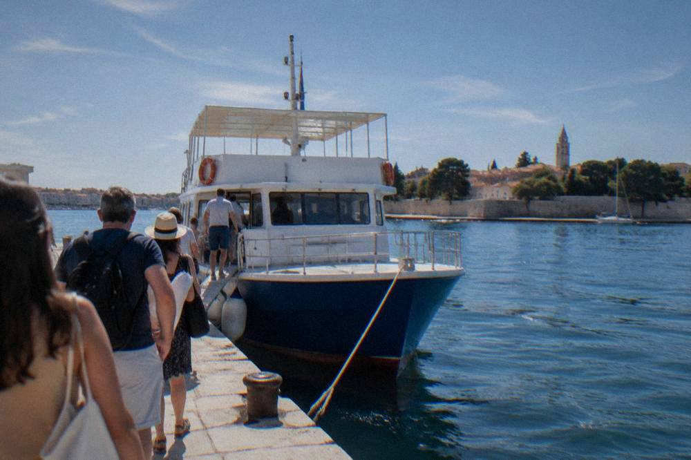 A tour boat tied at a dock with passengers seen from behind waiting to board.