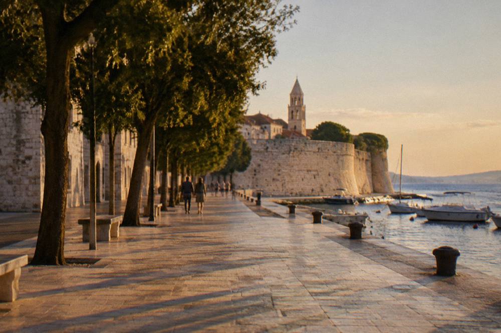 A tree-lined city street leading toward the Old Town walls in warm light.