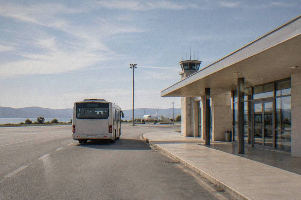 A shuttle bus pulling away from a small airport terminal on a clear day.