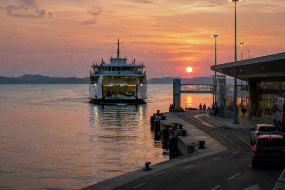 A car ferry approaching a modern ferry terminal at dusk over calm sea.