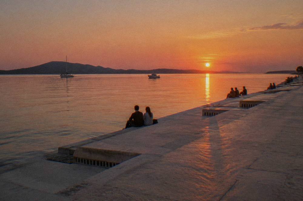 A few distant people on stone quay steps at sunset beside the sea.