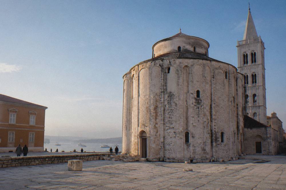 The round stone exterior of the ninth century Church of St Donatus against a blue sky.