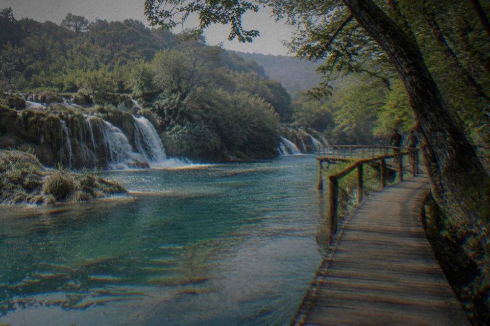 A wooden walkway curving over turquoise lakes in a forest with small cascades.