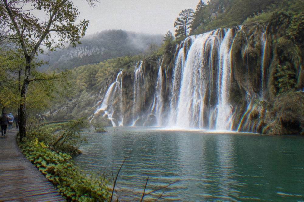 A wide waterfall spilling over travertine barriers into a green pool.