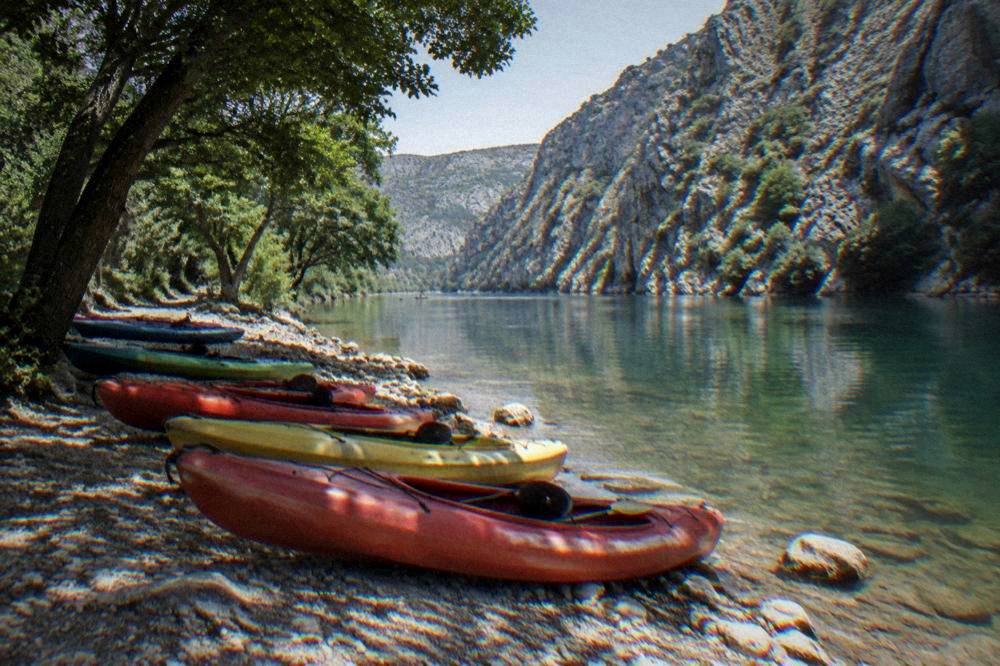 Kayaks lined up on a riverbank beside clear green water in a limestone gorge.