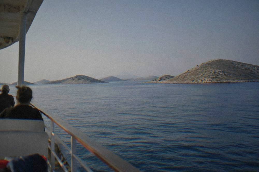 A line of barren stone islands in a calm blue sea seen from a boat deck.