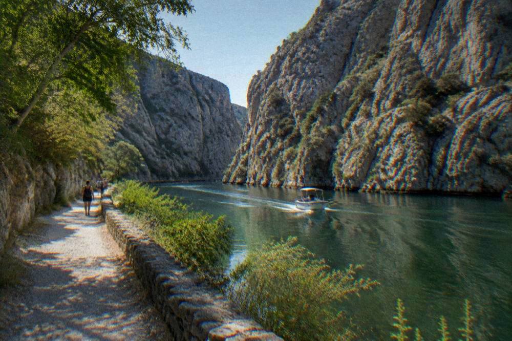 A canyon with sheer grey cliffs above a walking path beside a green river.