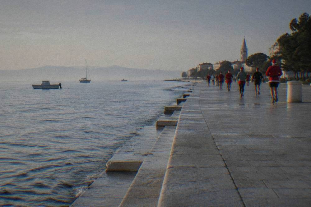 Distant runners in festive clothing moving along a seaside promenade.