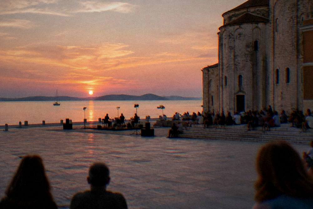 A distant audience seated on stone steps of a historic building for an evening show.