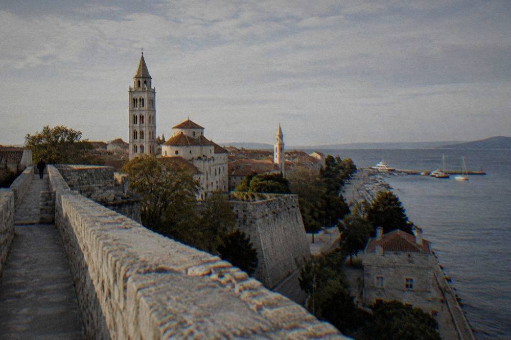 Empty stone alleys and church towers seen from a high bastion wall in soft light.