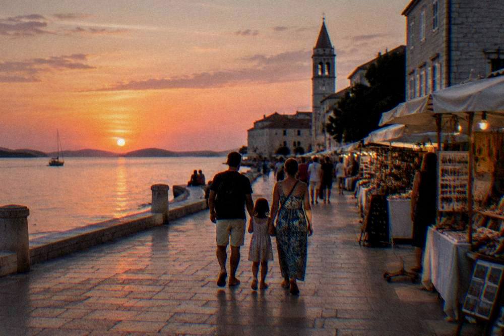 A family seen from behind walking past softly lit stalls in an old town square.