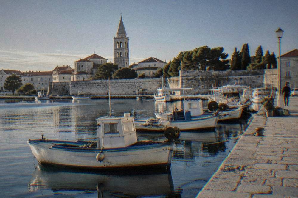 Fishing boats and a stone quay in morning light with a church tower behind.