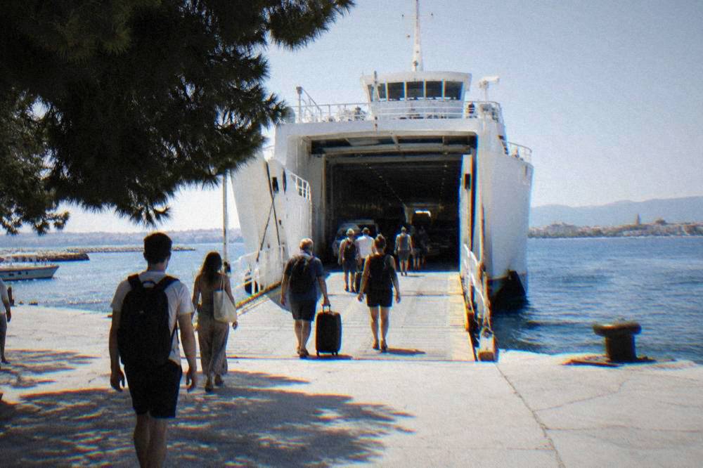Passengers seen from behind walking up the ramp of a white car ferry.