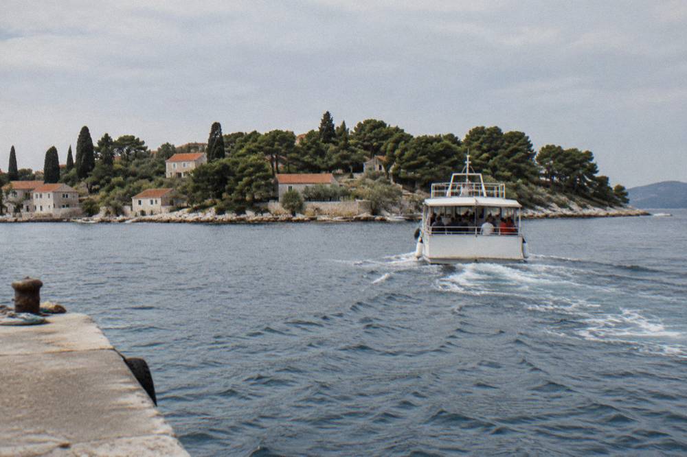 A small passenger ferry crossing a narrow channel toward a pine-covered island.
