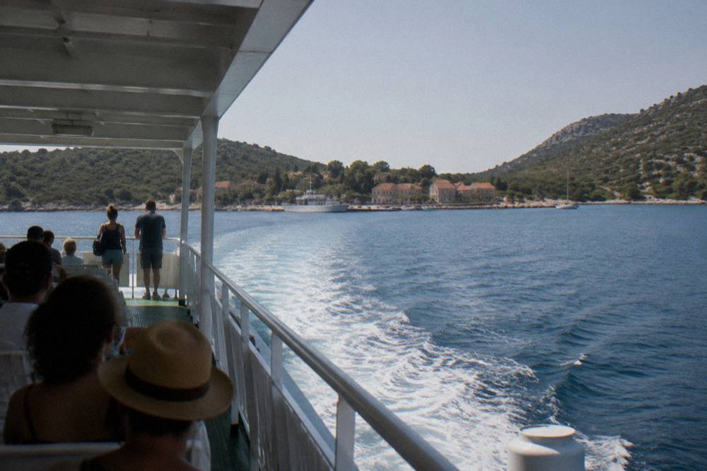 Distant passengers on a sunny ferry deck seen from behind as the boat leaves.