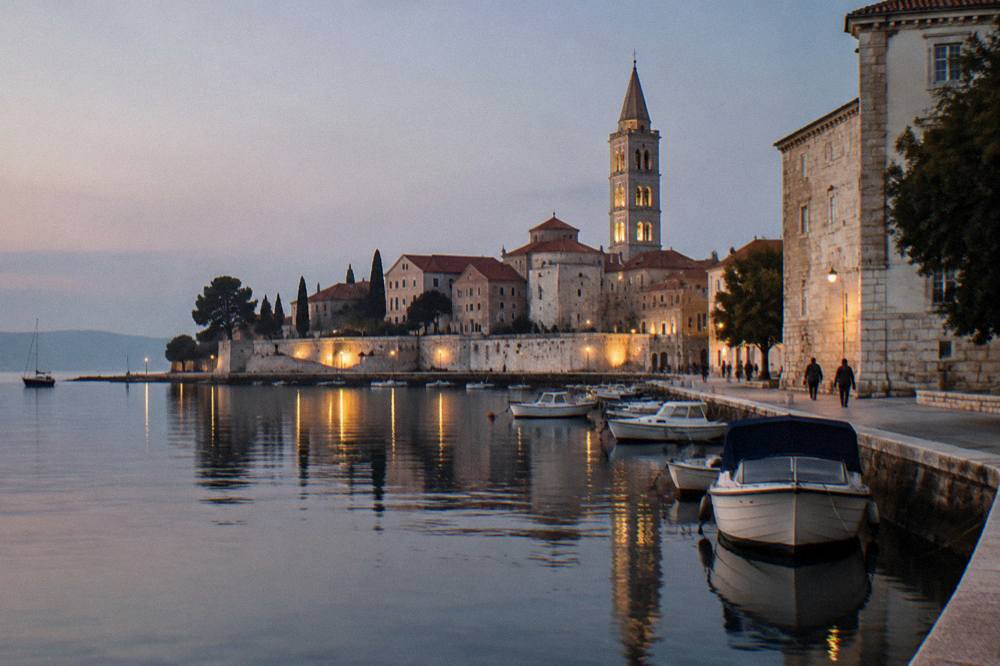 The lights of Zadar Old Town reflected in still harbour water at night.