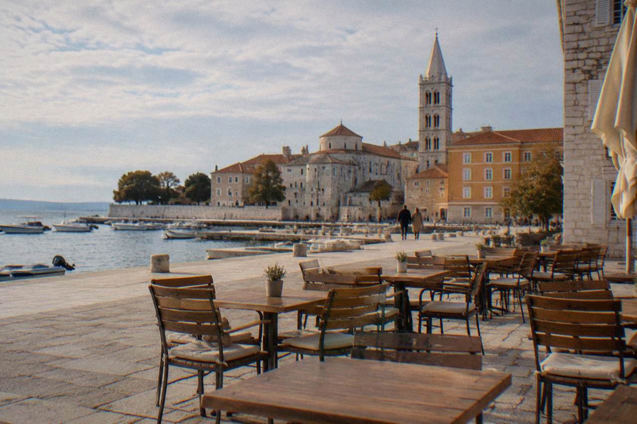 Empty cafe tables on a limestone square in Zadar old town beneath a bell tower.