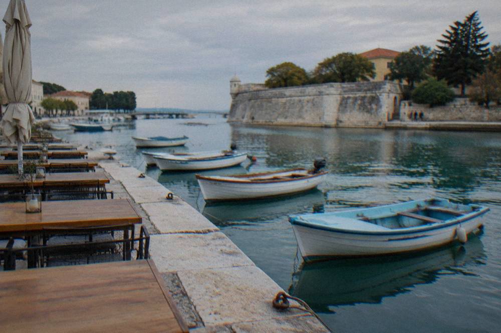 Small rowboats on calm water beside a waterfront restaurant terrace at Foša harbour in Zadar.