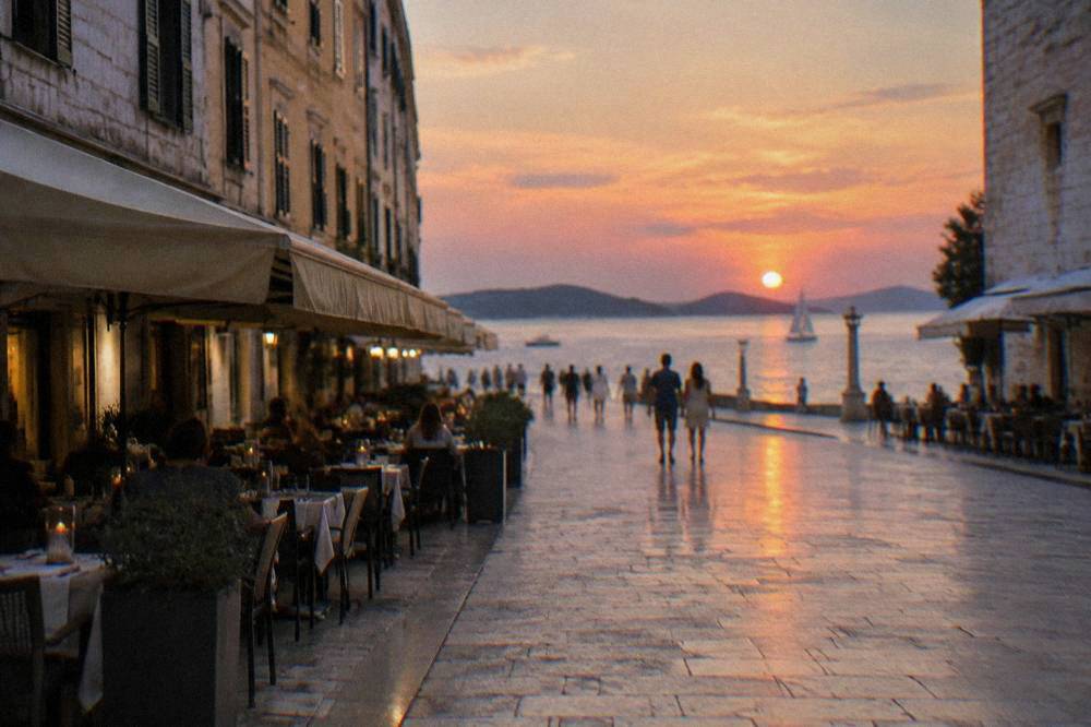 Restaurant tables lining the polished limestone pedestrian street of Kalelarga in Zadar at golden hour.