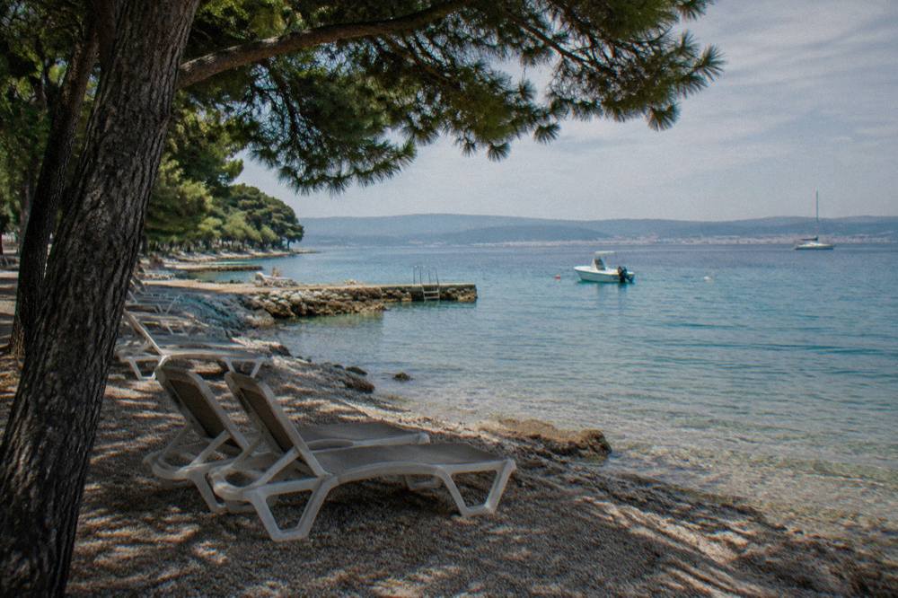 A pine-shaded pebble beach with calm turquoise water at Borik in Zadar.