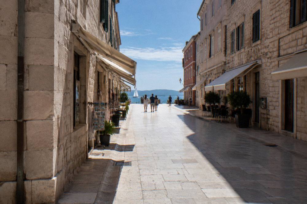 The limestone street of Kalelarga in Zadar at midday with awnings and long shadows.