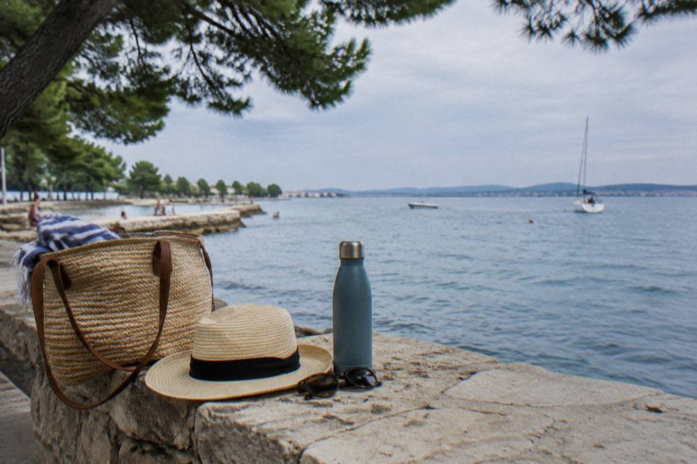 A sun hat, sunglasses and water bottle on a stone ledge beside the sea in Zadar.