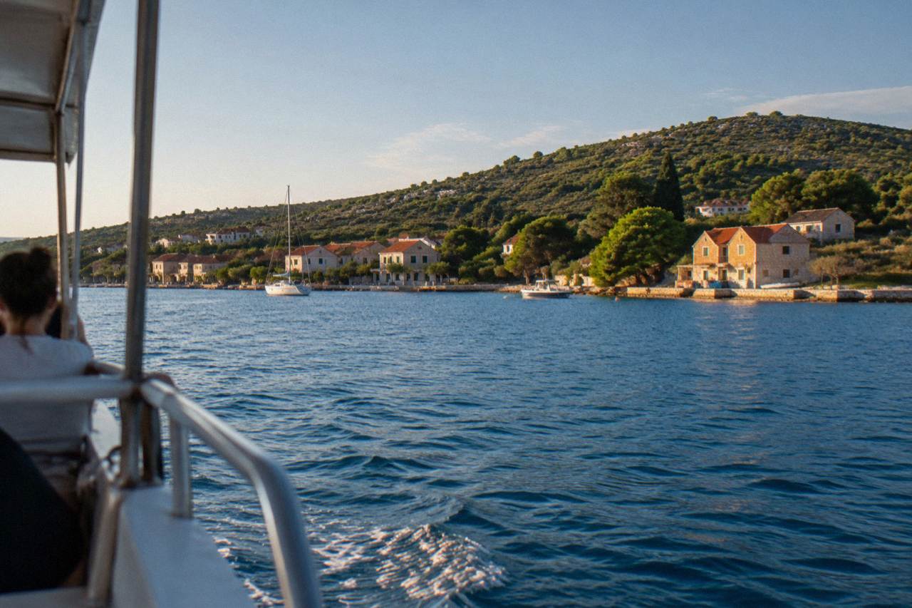The green coast of Ugljan island seen from the water across a calm blue strait.