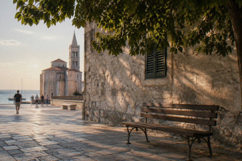 A shaded bench and stone wall on People's Square in Zadar.