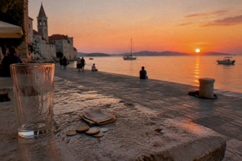 Coins on a worn stone ledge beside an empty glass in Zadar old town.