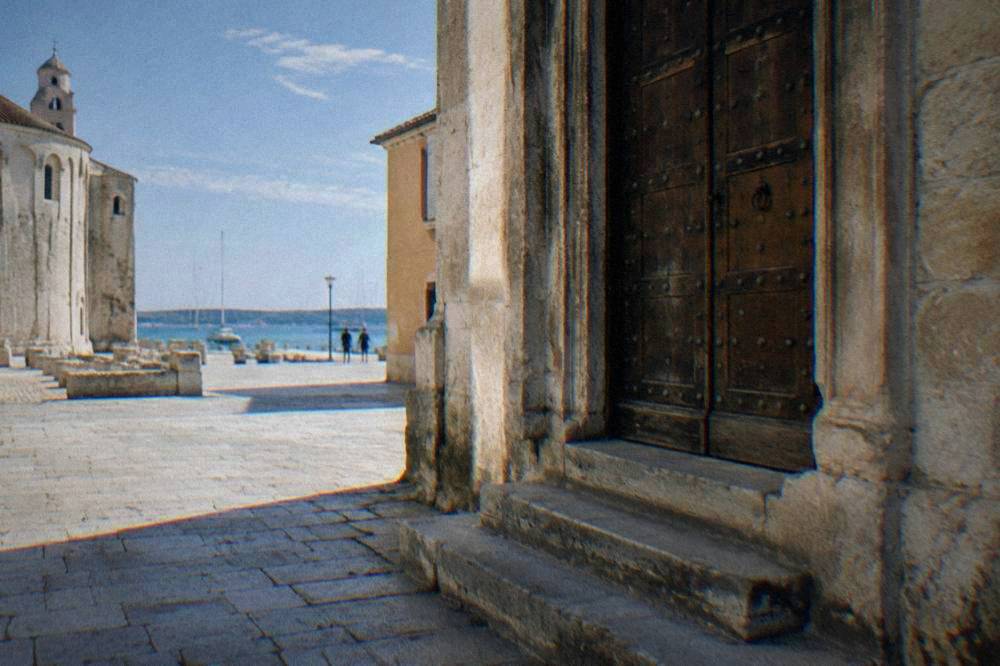 A heavy wooden museum door with worn stone steps on a quiet lane in Zadar.