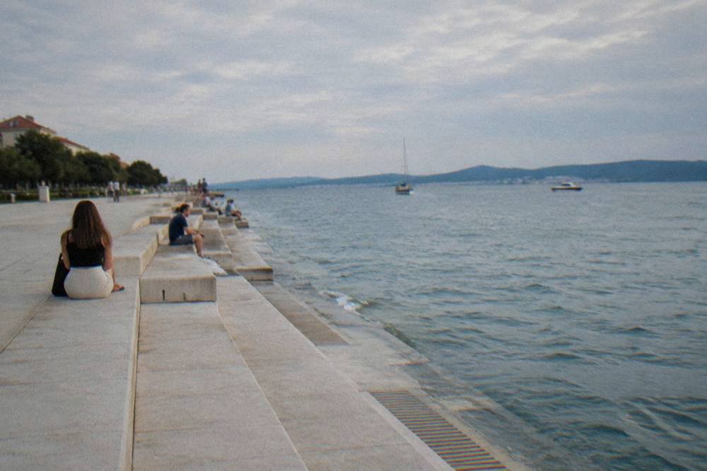 Waterfront promenade by the Sea Organ with calm sea and distant people sitting on the steps.