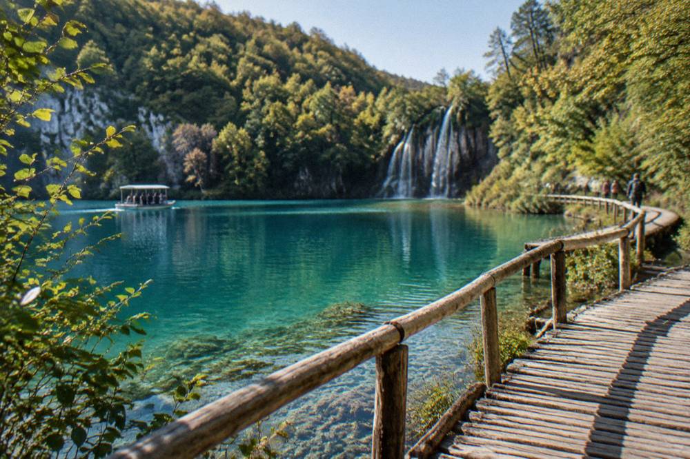 A wooden walkway over a turquoise lake with forested slopes at Plitvice Lakes.
