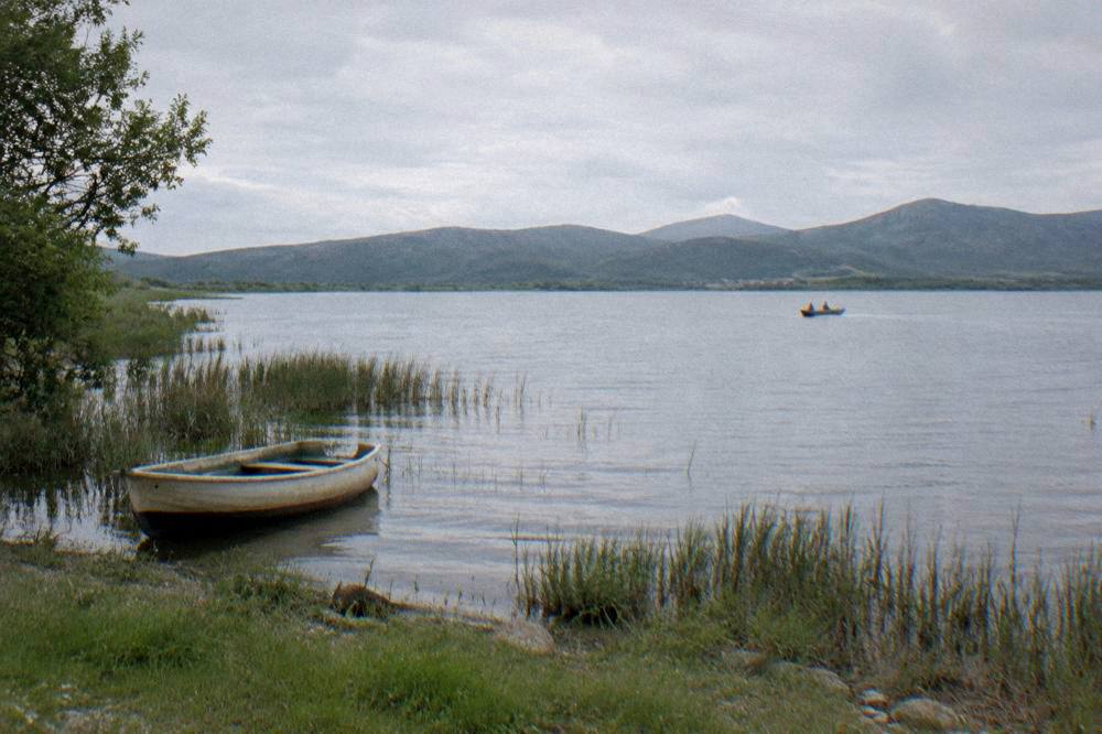Calm Vransko Jezero lake with reeds, green shore and distant hills.