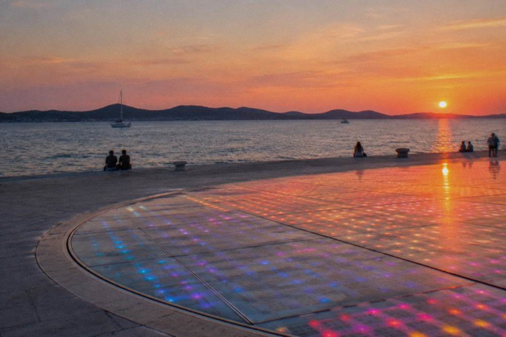The lit circular glass surface of Greeting to the Sun beside the sea at dusk in Zadar.