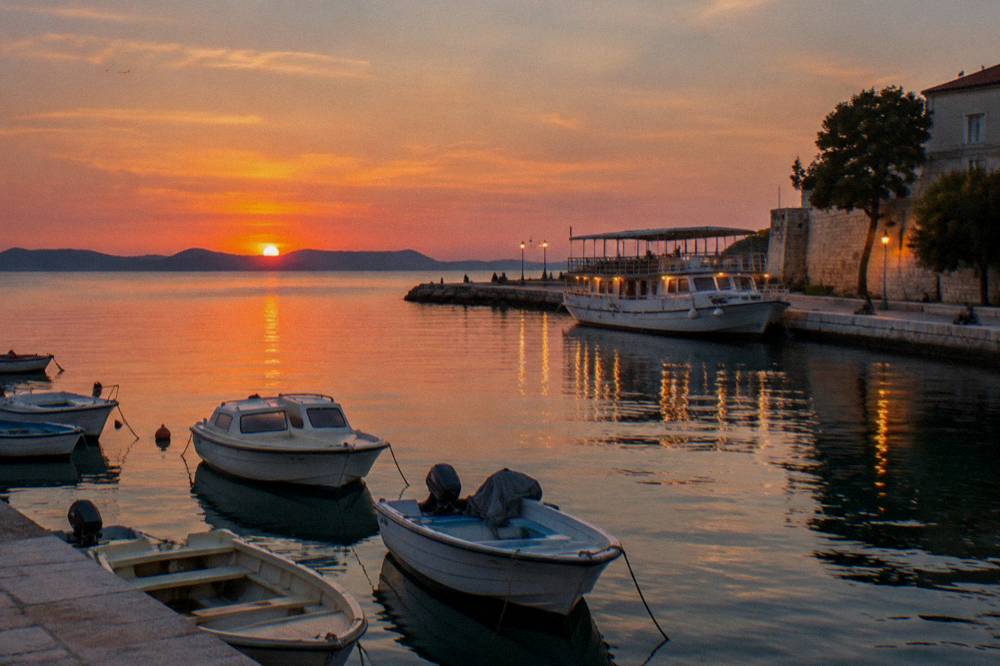 Boats and warm lights reflected in calm water at Foša harbour at dusk in Zadar.