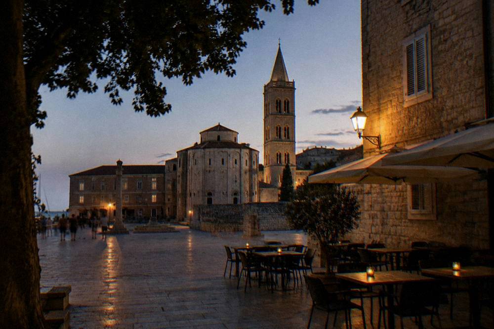 A quiet night on People's Square in Zadar with a warm lamp and empty tables.