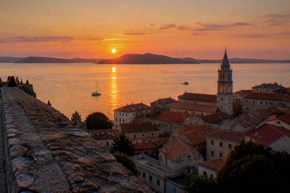 Terracotta roofs and a bell tower of Zadar old town seen from a high bastion wall at golden hour.