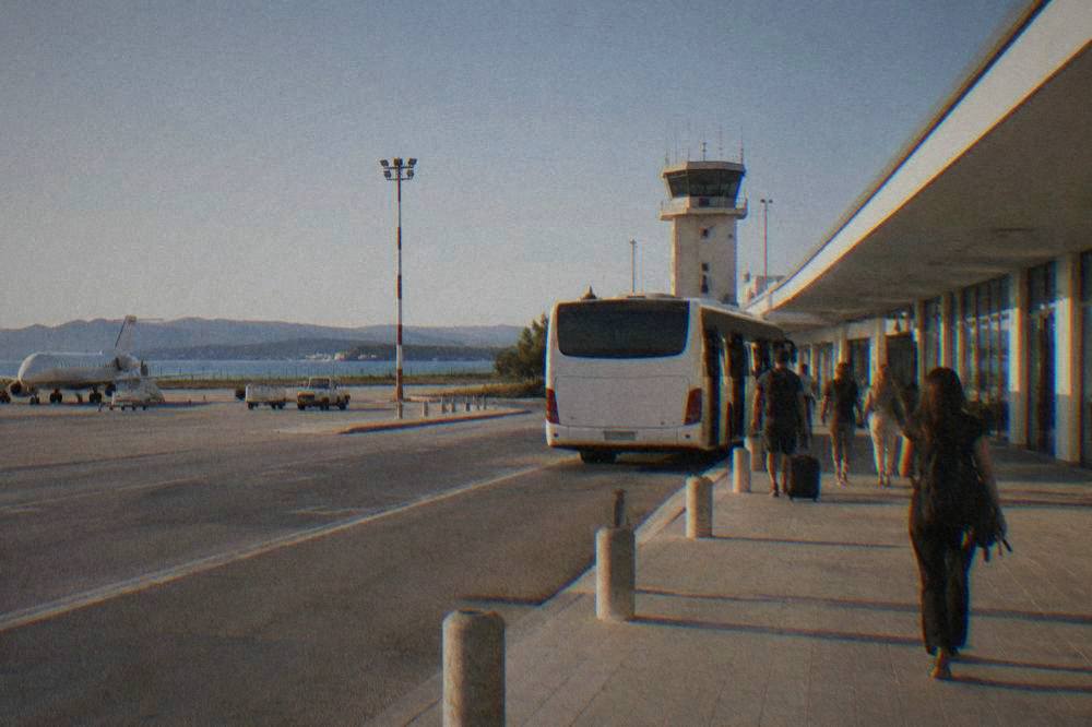 A shuttle coach at the kerb of Zadar airport's low terminal under clear sky.