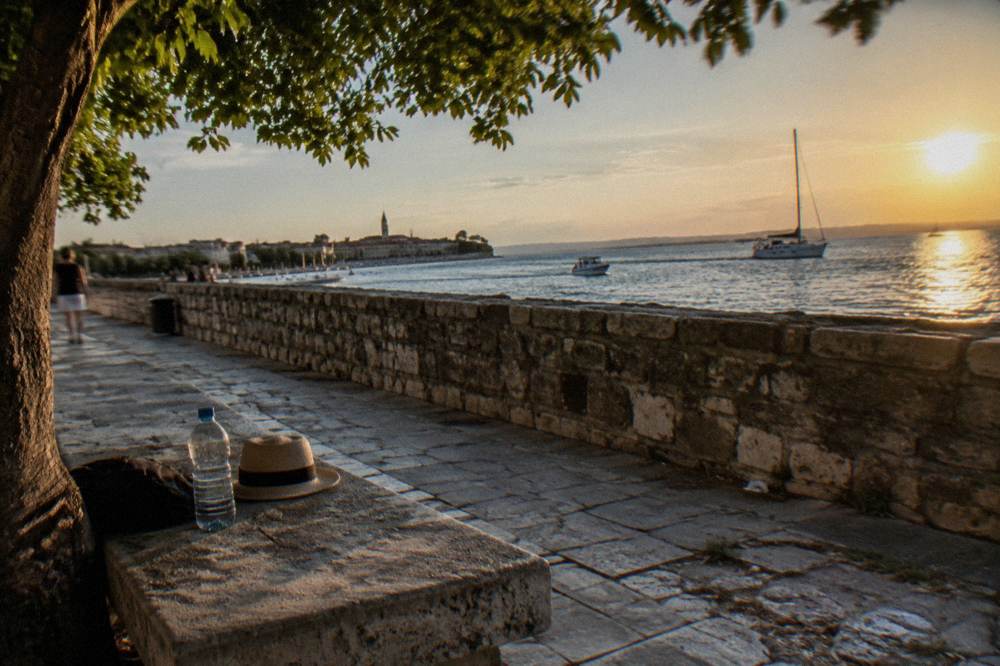 A shaded bench on the old walls promenade in Zadar with the sea beyond.