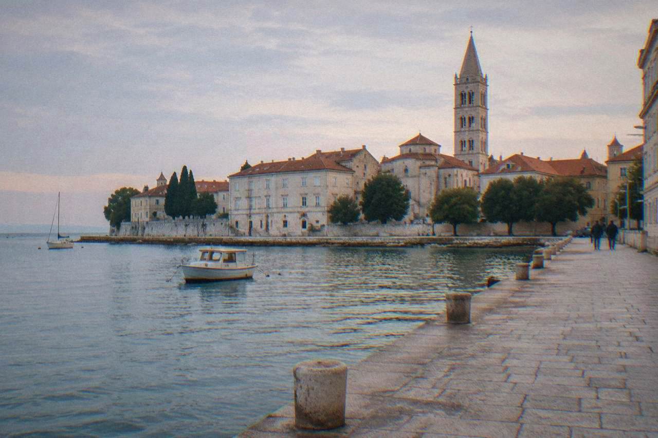 Zadar old town waterfront at dawn with terracotta roofs and bell tower.