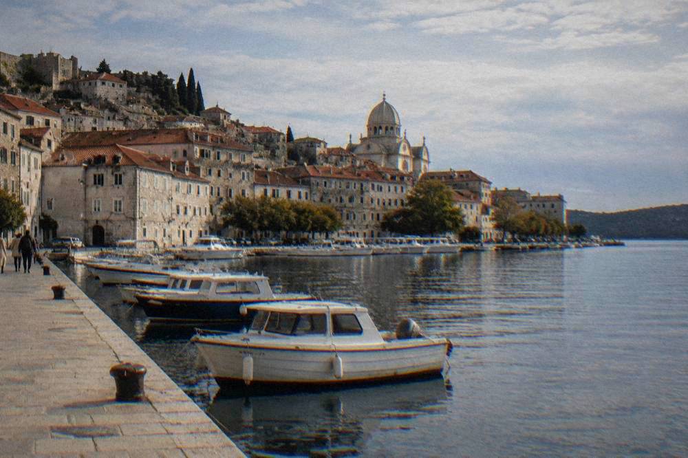 Šibenik's harbour with pale stone houses, a cathedral dome and moored boats.