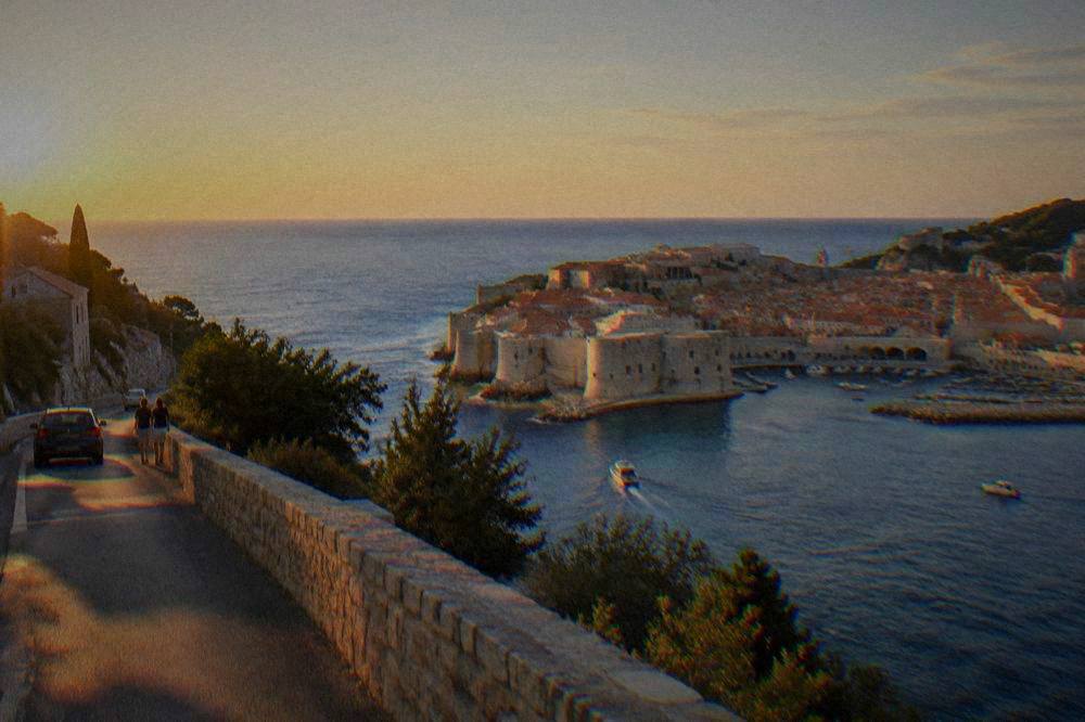 Dubrovnik's pale stone walls and red roofs over deep blue sea from a hillside road.