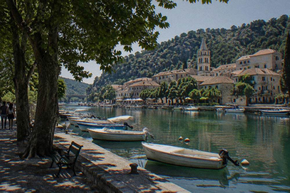 Skradin riverside town with moored boats and stone houses by calm green water.