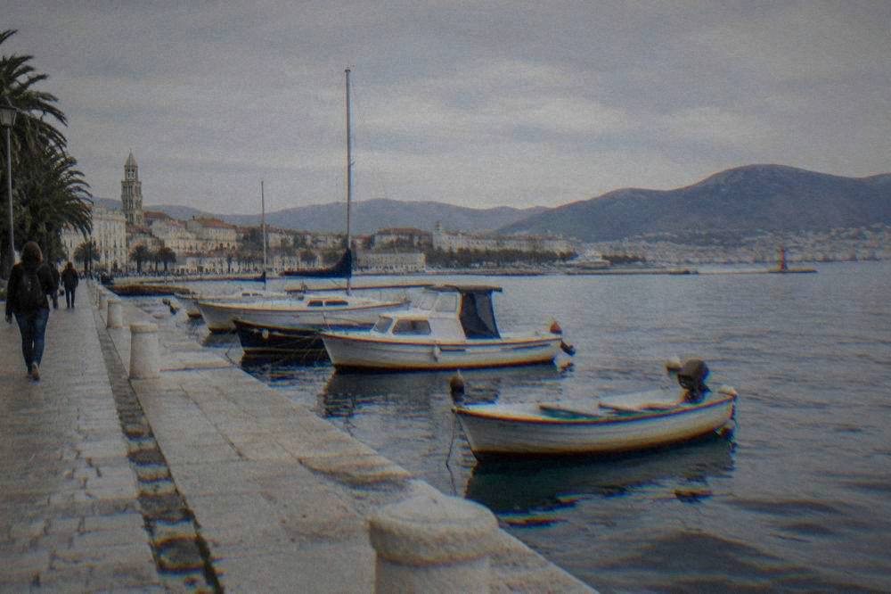Split's stone harbour wall and moored boats on the calm Adriatic with hills behind.
