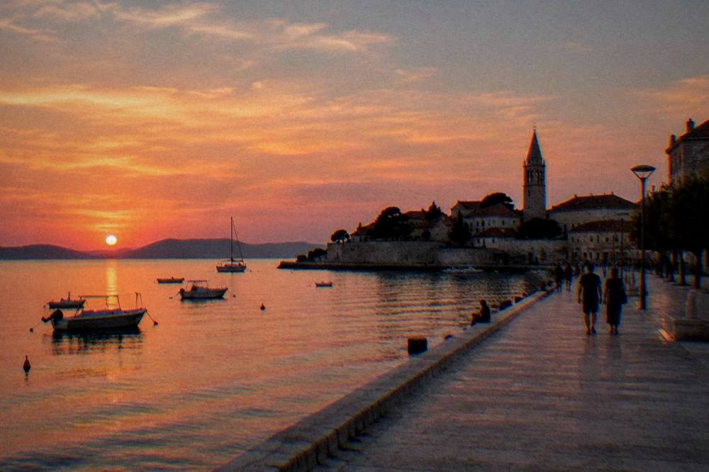 Sunset over the Zadar waterfront with the bell tower and terracotta roofs silhouetted.