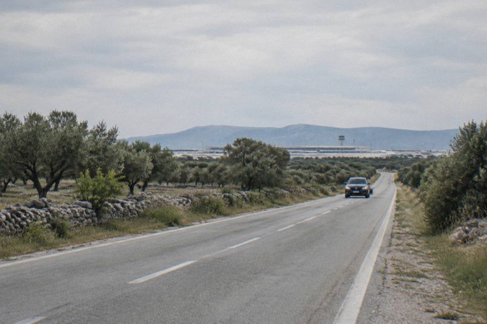 A car on a quiet road near Zadar airport with olive trees and dry fields beside it.
